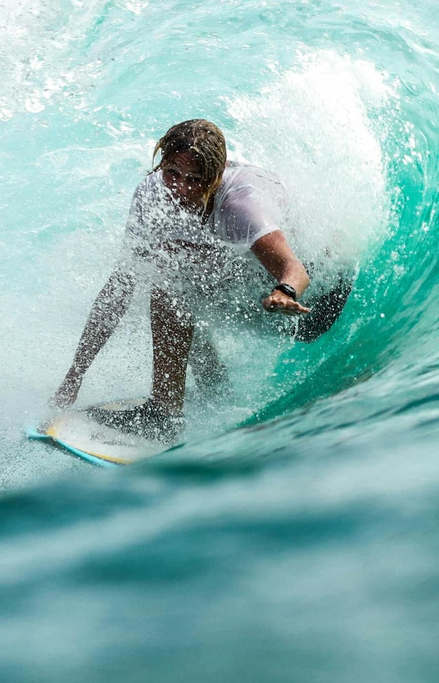 A surfer crouched inside the barrel of a turquoise wave.